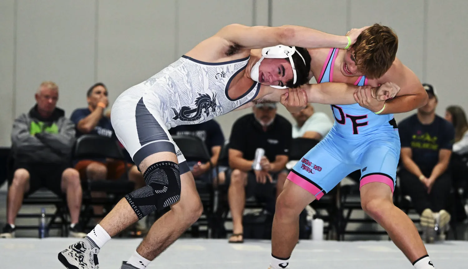 Two wrestlers locked in a tie-up in custom sublimated singlets