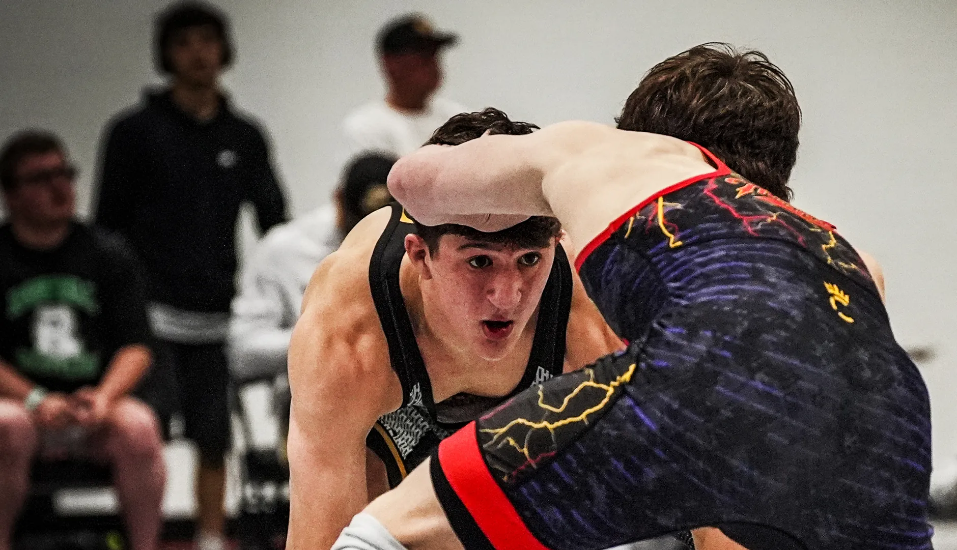 Two wrestlers hand-fighting on the mat, one looking straight at the camera